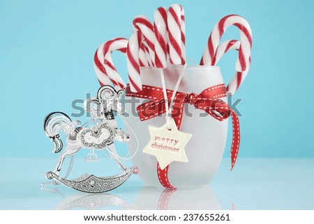 Merry Christmas silver vintage rocking horse tree ornament and jar of red and white candy canes on pale aqua blue and white background.