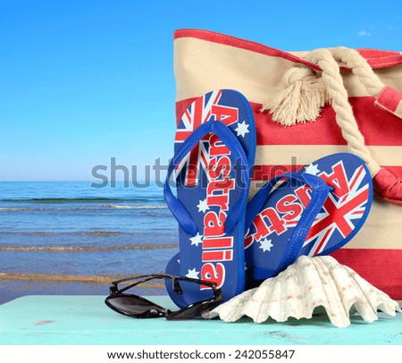 Australian beach scene with Aussie sandals, beach bag, sunglasses and shell with view of blue ocean.
