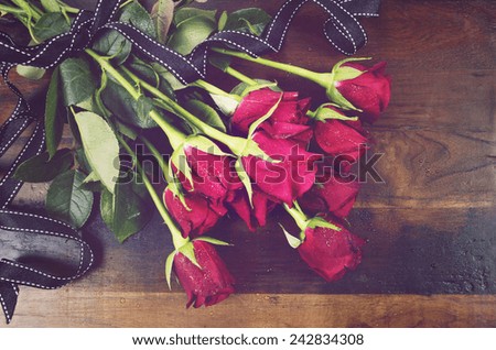 Retro vintage Valentines Day red roses on dark recycled wood background - overhead with black ribbon.