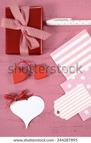 Wrapping Happy Valentines Day gifts with gift tags and hearts on shabby chic pink background - vertical.