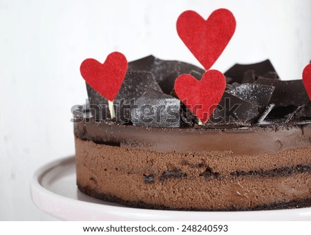 Valentine chocolate mousse layer gateau cake with chocolate shards decoration and red hearts on shabby chic vintage white and pink wood background.