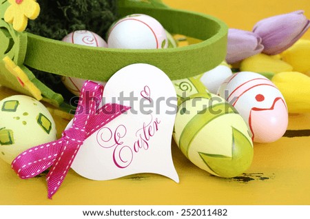 Happy Easter green and yellow felt basket of of pink, white and green easter eggs on rustic vintage yellow wood table, with heart shape greeting card, closeup.