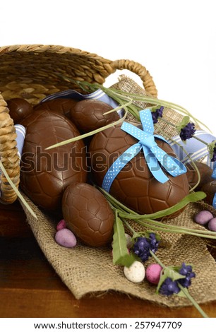 Happy Easter basket hamper of chocolate Easter Eggs and flower on dark wood table.