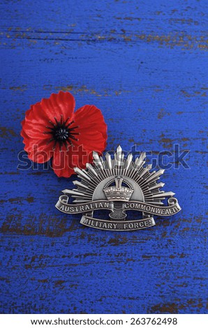 ADELAIDE, AUSTRALIA - MARCH 18, 2015: Australian Anzac WWI rising star hat badge with red Remembrance poppy on dark blue wood background.