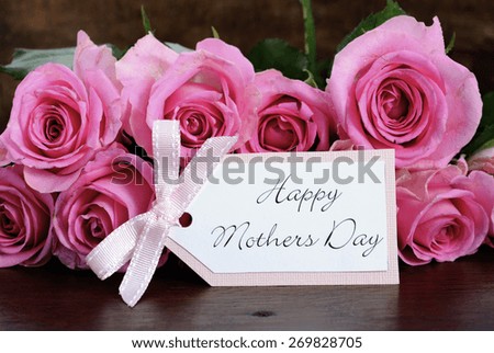 Mothers Day pink roses on rustic dark wood table with greeting gift tag, closeup.