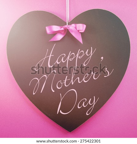 Happy Mothers Day message written on a black blackboard with blue ribbon against a blue background, with applied retro style filters and added lens flare light beam.