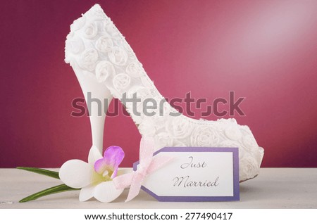 Wedding June Bride concept with white floral high heel shoe and frangipani flower on white shabby chic table and marsala color background, with applied retro filters and added lens flare.