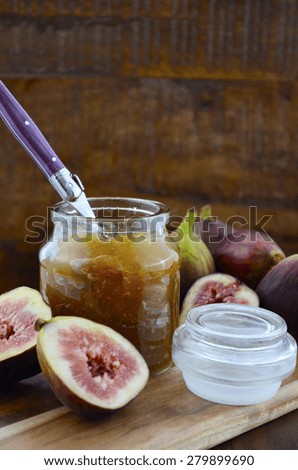 Fresh figs on wooden cutting chopping board with jar of fig jelly preserve on dark wood rustic table background.