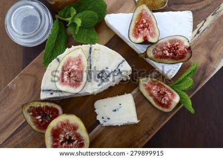 Fresh figs on wooden cutting chopping board with jar of fig jelly preserve and gourmet cheese on dark wood rustic table background, overhead view.