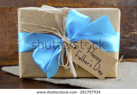 Happy Fathers Day natural kraft paper wrapped gift with pale blue ribbon on dark wood background.