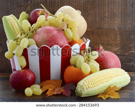 Red and white stripe bowl with Autumn Harvest fruit and vegetables on dark vintage wood background.