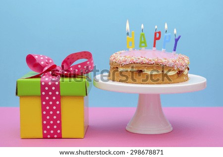Bright color gift box with cake and candles on modern pink and blue background.