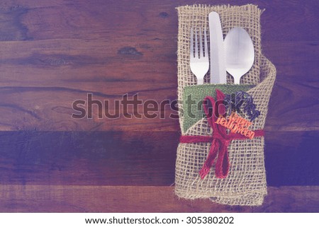 Rustic Halloween table place setting with burlap wrapped cutlery on dark wood table with applied retro vintage filters.
