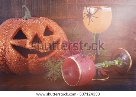 Happy Halloween table with Jack O Lantern pumpkin with party wine goblets on rustic dark wood vintage background with added vintage style filters and lens flare.