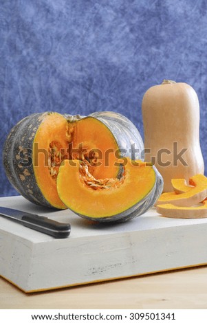Food Preparation for Autumn or Thanksgiving meal with cut pumpkin and butternut squash on large white wooden board in blue and white kitchen theme.