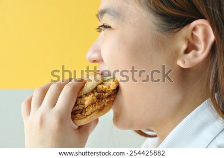 Asian woman age 28 years old in uniform eating chicken burger, junk food.