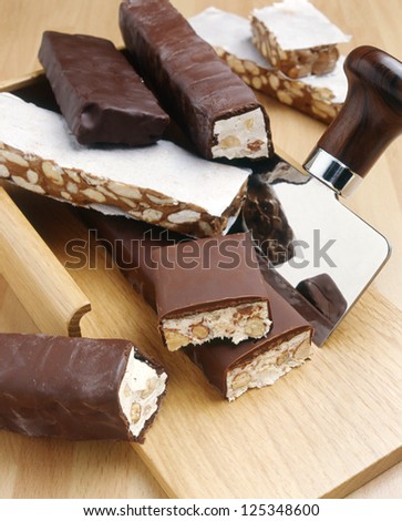 A variety of different nutty nougat in dark chocolate with roasted hazelnuts cut open to show the nougat mix on a wooden board with a stainless steel blade