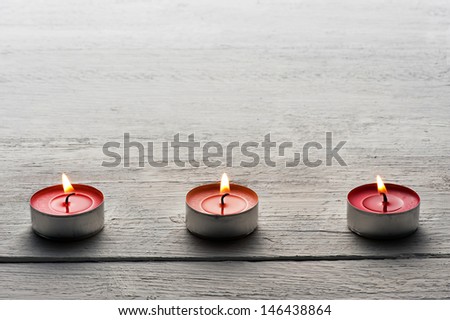 Row of burning red tea lights or small candles on a dark wooden surface with copy space above