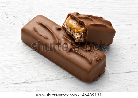 Chocolate candy bar with a delicious soft nougat center with one whole bar and one broken open to display the filling on a white textured background