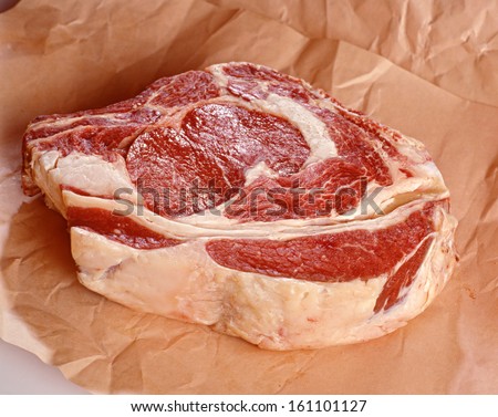Raw rib steak with marbled meat and fat displayed on a sheet of crumpled brown paper