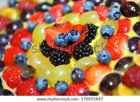 Colorful fresh fruit topping on a cake with assorted berries including blueberries, strawberries and blackberries, with green and black grapes arranged in concentric circles