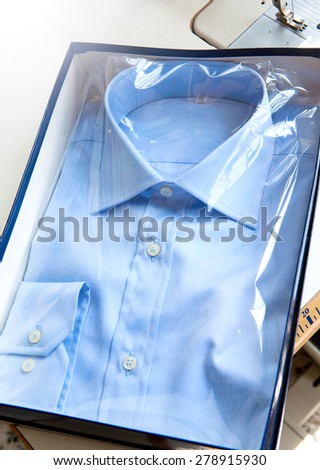 New light blue elegant shirt for men with white buttons and long sleeves designed in classical fashion style, folded in a transparent plastic pack for sale, close-up