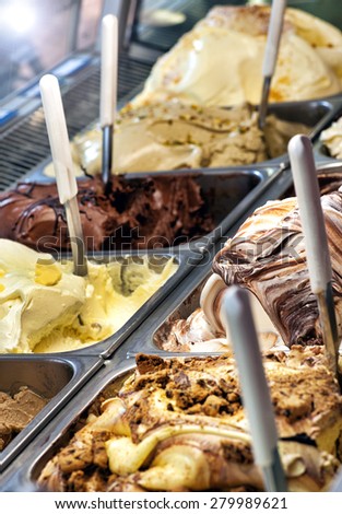 Variety of delicious freshly prepared ice cream flavors on display in metal trays in a shop or ice cream parlour for sale as takeaway summer snacks, close up view with scoops ready to serve