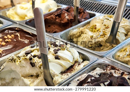 Close up of trays of different ice cream in assorted flavors displayed in a store window in metal trays with scoops for takeaway summer snacks
