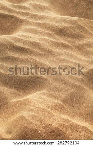 Windblown sand background with an uneven rippled surface created by the force of the wind showing the grainy texture of the sand