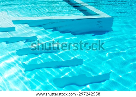 Underwater steps in a sparkling blue swimming pool with reflections of the summer sunlight, background image for vacation themed concepts