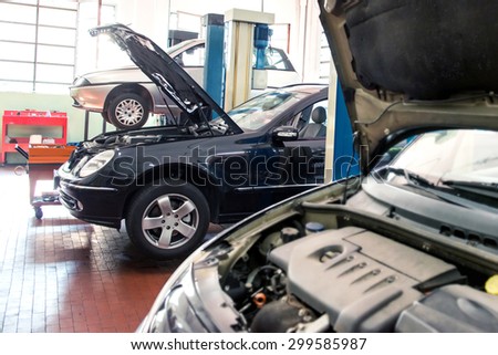 Three cars in an automotive repair shop undergoing maintenance, repair and service, one on a hoist and two with the engine compartments open