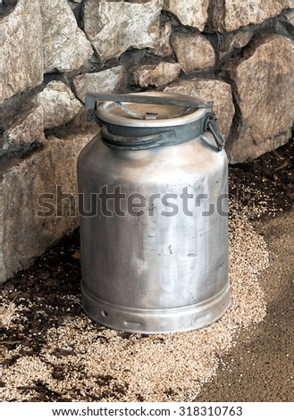 Old vintage metal aluminum milk churn, urn or can used on a dairy farm with its lid in place displayed against a natural rock wall, high angle view
