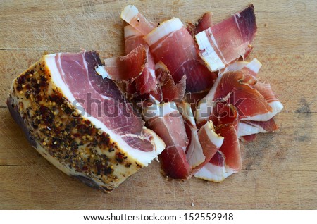 Homemade spicy prosciutto, smoked and dried in the wind for a long time on wooden chopping board, big piece and thin slices against white background