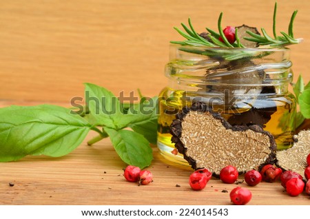 Sliced heart shaped black truffle in olive oil in small jar and some fresh spices, basil, oregano, rosemary and red pepper, close up view