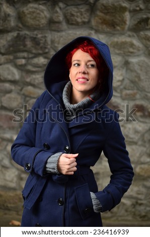 Young, beautiful redhead girl posing  in gray sweater and blue coat with large hood