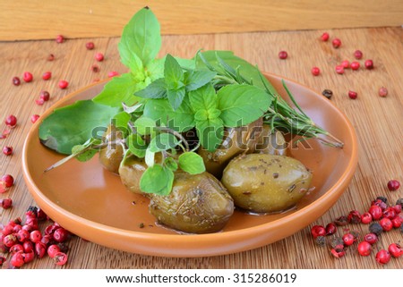 Aromatic green olives in rustic ceramic saucer, decorated with green basil, oregano, rosemary, pepper and mojito mint leaves and red pepper, on wooden background