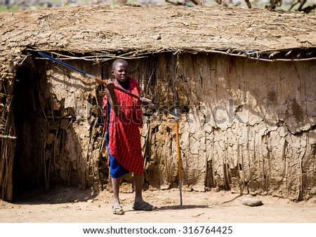 Tanzania 2015 Year January 26 .Masai village . Small  village boy with a spear against a traditional house