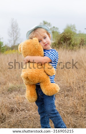Cute little girl standing in the grass hugging a Teddy bear
