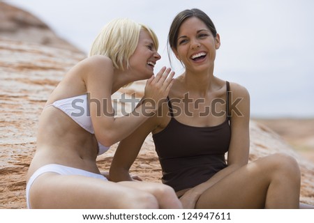 Two female friends in bikinis laughing on the beach