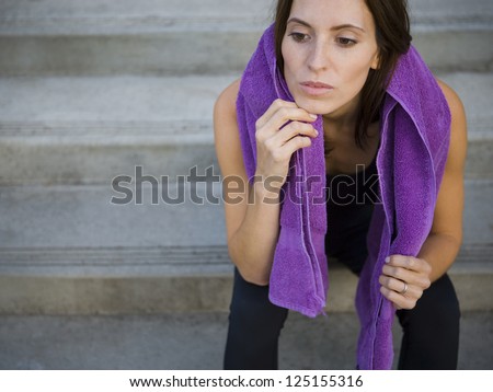 Female jogger sitting on steps with towel in her neck