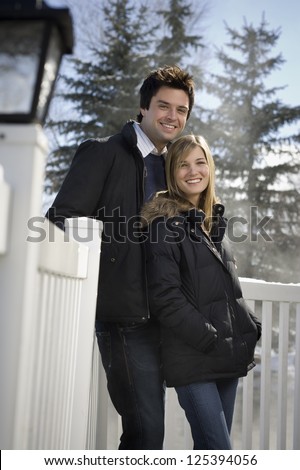 Three quarter length of a young couple leaning against white fence