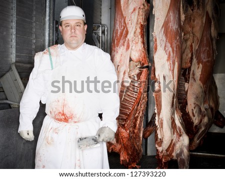 Butcher standing with hanging carcass and knife