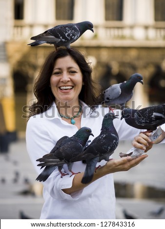 Woman in public square feeding pigeons and smiling