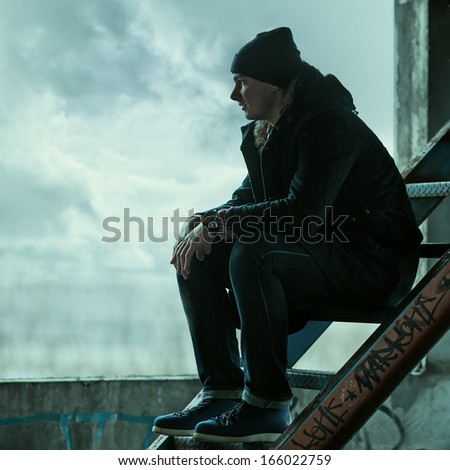 Trendy man sitting on the stairs and looks into the distance