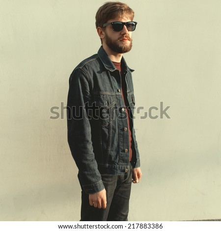 A man with a beard wearing glasses, a white wall in a sunny day