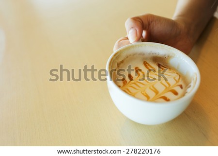 woman hand holding coffee cup caramel macchiato hot of coffee drink on wooden table in the cafe