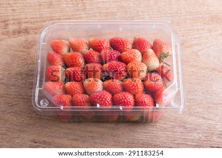 red ripe strawberry in plastic box of packaging on wood table