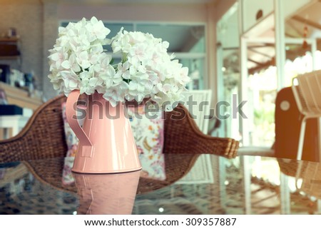 white plastic flowers in pink flower vase on the rattan weave table decorated interior in cafe