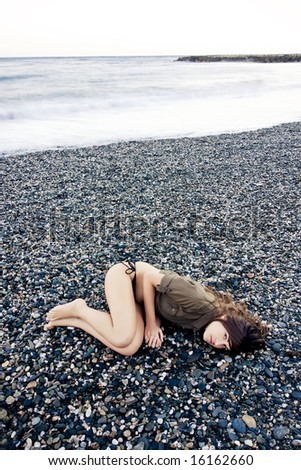 Beautiful woman laying on the beach with sad gesture. Long exposed waves.