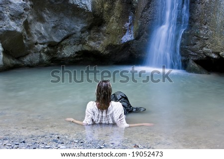 Young blond woman swimming in waterfall lake.